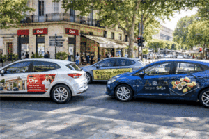 Plusieurs véhicules marqués qui se déplacent dans une rue avec les logos d'annonceurs sur les portes latérales.